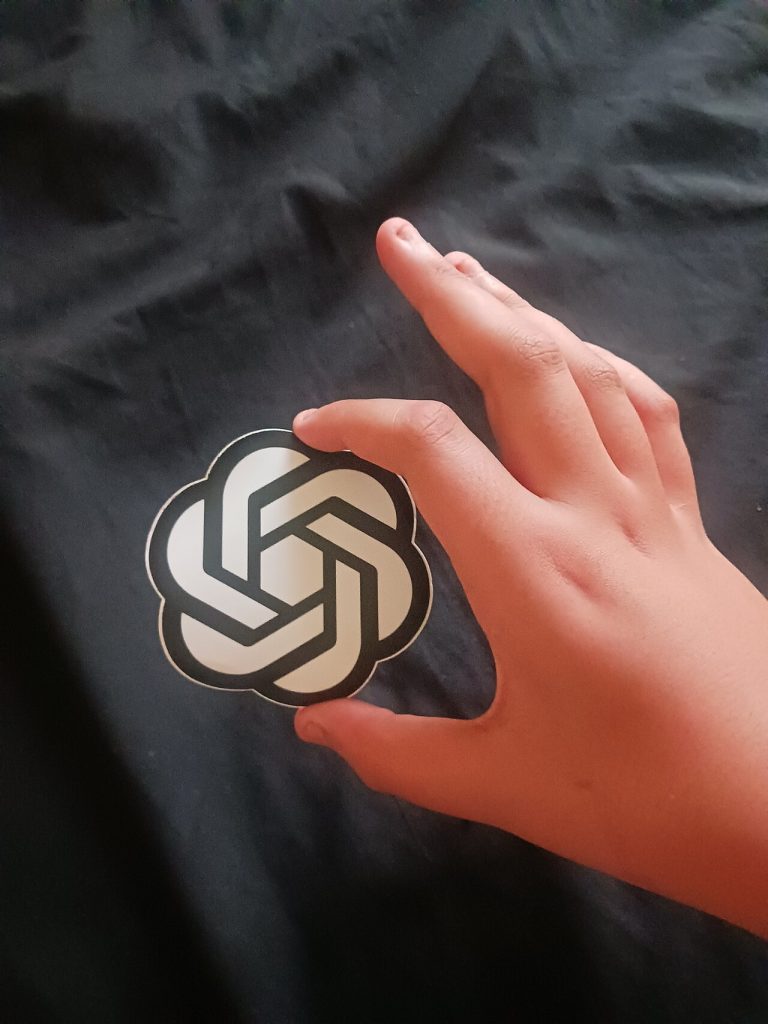 This image is of a hand holding the OpenAI sticker, symbolizing use of ChatGPT.