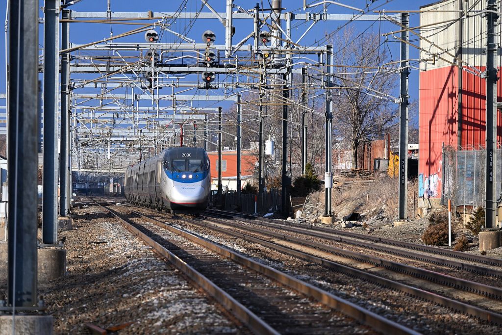 Southbound Amtrak Acela Express train #2275 approaches Readville station on track 1. The rear of northbound Amtrak Northeast Regional train #164 can be seen in the background.
