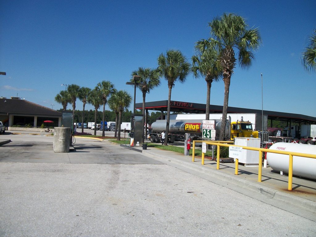 A Peterbilt, Pilot Travel Center tanker truck adding diesel fuel and being cleaned off by the driver at the Flying J Travel Plaza off the northeast corner of Florida State Road 52 and Interstate 75 in Pasco, Florida, west of San Antonio, Florida. Flying J and Pilot Travel Centers merged with each other, hence this truck. This was taken from the uncanopied area for propane, gas, and diesel fuel pumps, and was supposed to be of the separate diesel fuel pump canopy for trucks. Cars and RV's get their fuel from where I was standing at the time.