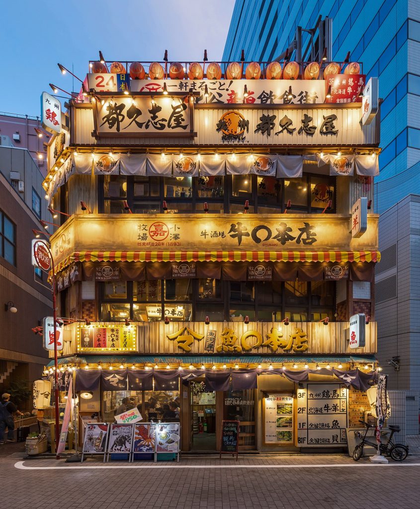 Illuminated facade of a 3-storey restaurant with Japanese signs and red paper lanterns, at blue hour, in Yūrakuchō, Chiyoda, Tokyo, Japan.