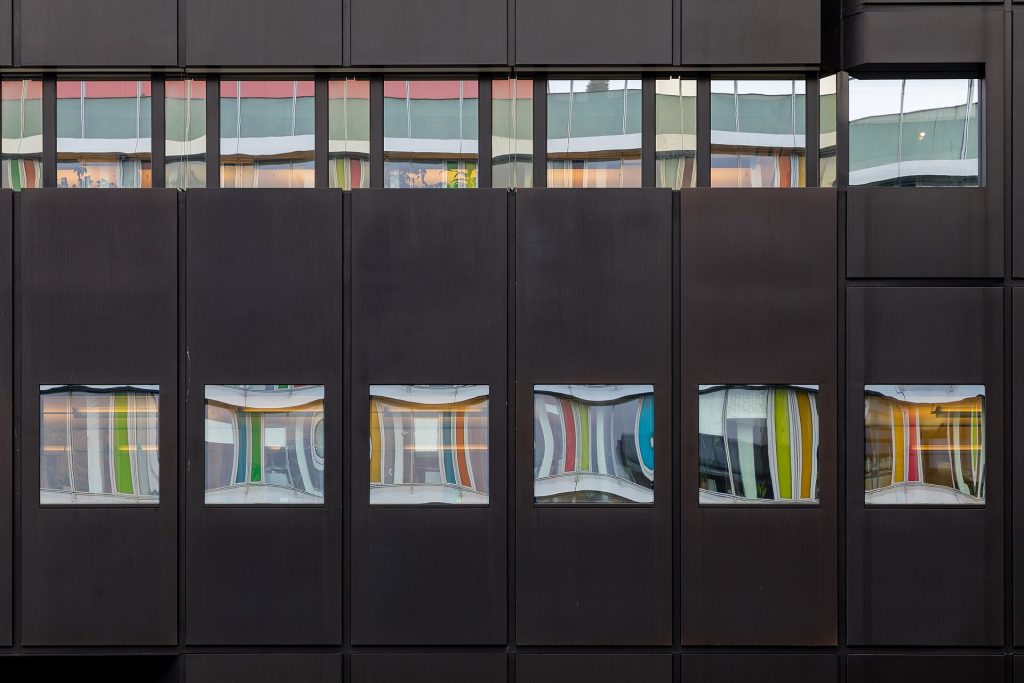 Facade of an office building of the Westdeutsche Lotterie, Münster, North Rhine-Westphalia, GermanyThe WestLotto headquarters in Münster is the main office of Westdeutsche Lotterie (WestLotto). An architectural competition was held in 1958 to design the headquarters, which was won by renowned Münster architect Harald Deilmann. The modern company building was constructed on a plot of land on Weseler Straße that was still undeveloped at the time and made a clear architectural statement for the development of a new service district in the city. Since its original construction, the building has been expanded and renovated several times.For the central building, Harald Deilmann used a clearly structured grid that is both urban and functional and is reflected in both the façade and the interior design. The façade combines black glazed clinker bricks with aluminum windows, giving the building a distinctive appearance in the urban context despite its functionality.In 1978, the building was given a striking black tower, which further developed the architectural design language. In 1994, the administration building was raised, contributing to a change in its silhouette.