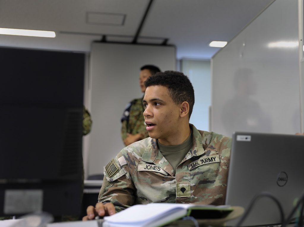 U.S. Army Spc. Makai Jones, assigned to the 1st Multi-Domain Task Force, converses with his team at Camp Itami, Japan, July 25, 2024. This cyber exchange involves collaborative efforts from the U.S. Army, JGSDF, and Australian Army to share intelligence, conduct joint cyber exercises, and enhance mutual cybersecurity defenses to protect against digital threats. (U.S. Army Reserve photo by Pfc. Arianna Zavala, 210th MPAD)