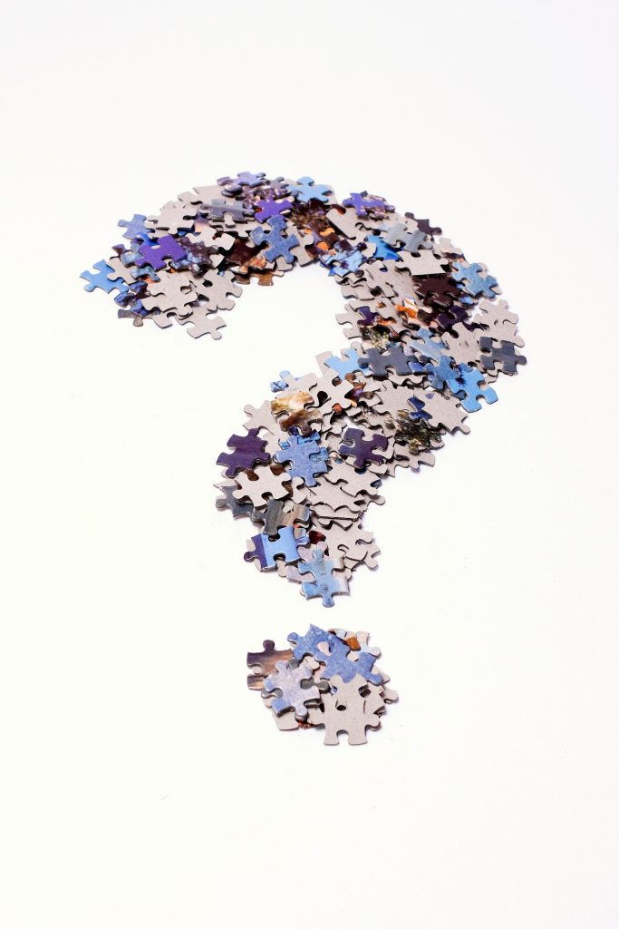 Question mark made of jigsaw puzzle pieces. A big question mark made by stacking various jigsaw puzzle pieces and then making them take that specific shape. The pieces are scrambled and on both sides against a white background.