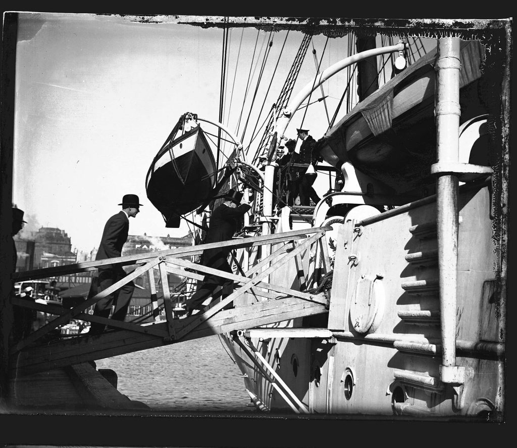 The GENERAL BAQUEDANO moored at East Circular Quay on 16 July 1931 and the crew spent two weeks in Sydney. The ship had previously visited Sydney in 1903. In 1931, the vessel was considered obsolete as a fighting ship, but very useful as a training vessel. In naval categories, GENERAL BAQUEDANO is known as a corvette (in Spanish corbeta), which is defined as a flush-decked ship with one tier of guns, a type replaced by the modern cruiser. Fully-rigged, the vessel was fitted with triple-expansion engines as auxiliary, and had a displacement of 2,330 tons. The visit attracted significant public interest and the daily activities of the Chileans were reported in the Sydney Morning Herald. The crew played a soccer match against members of the HMAS CANBERRA crew, laid a wreath at the Martin Place cenotaph, displayed their rigging skills while aloft and opened their vessel to the public. Captain Alvarez also hosted visits by the Governor of NSW Sir Phillip Game, the Premier of NSW and the Lord Mayor. The departure of GENERAL BAQUEDANO from Sydney Harbour was quite eventful, with one rating attempting to desert the ship and swim ashore, two sailors being left at the dock and transported to the vessel by police launch and another bewildered Chilean was found wandering the streets. He was later reunited with his fellow sailors in Auckland after transport was arranged on a departing cargo ship. This photo is part of the Australian National Maritime Museum’s Samuel J. Hood Studio collection. Sam Hood (1872-1953) was a Sydney photographer with a passion for ships. His 60-year career spanned the romantic age of sail and two world wars. The photos in the collection were taken mainly in Sydney and Newcastle during the first half of the 20th century. The ANMM undertakes research and accepts public comments that enhance the information we hold about images in our collection. This record has been updated accordingly. Photographer: Samuel J. Hood Studio Collection Object no. 00034752