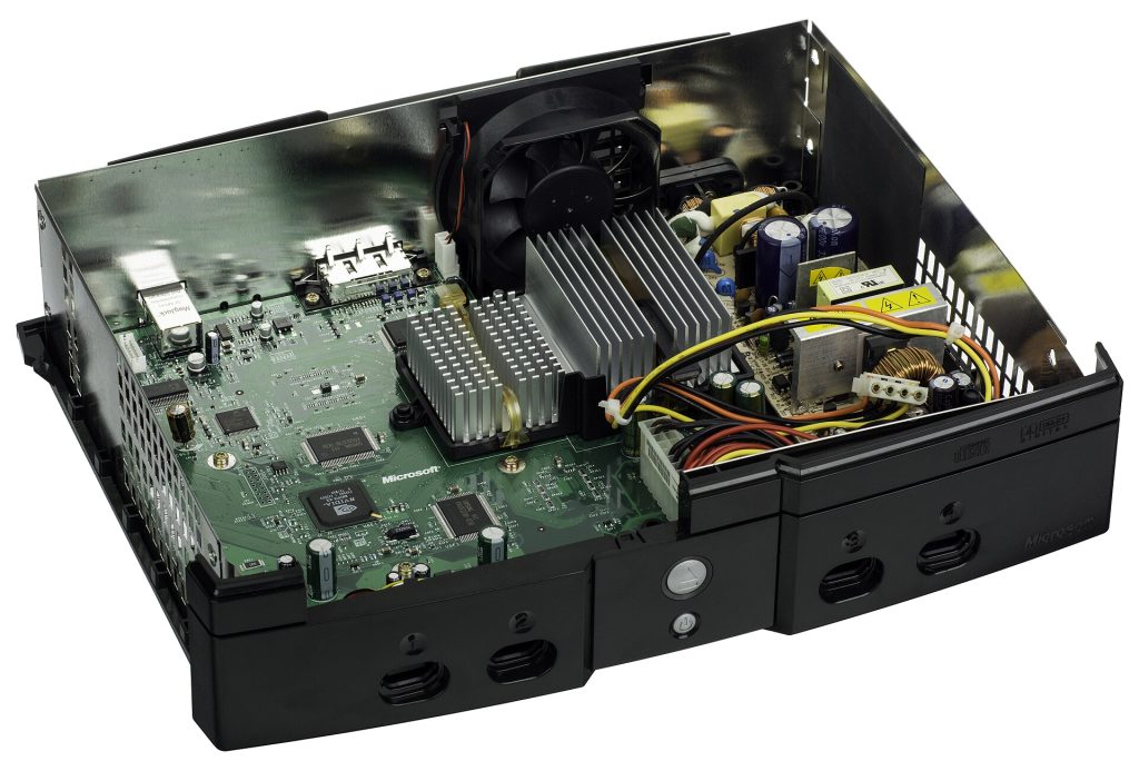 The inside of an Xbox, a sixth-generation gaming console made by Microsoft that was first released in 2001. The Xbox was Microsoft's first foray into the gaming console market, and was followed by the Xbox 360 in 2005. This picture shows the inside of console with the DVD and hard drives removed. The console shown is the 1.6 hardware revision, which was the last version of the console hardware that featured component reduction and streamlining. Manufacture date of the console is 2004-11-18, making this one of the last Xbox consoles made.