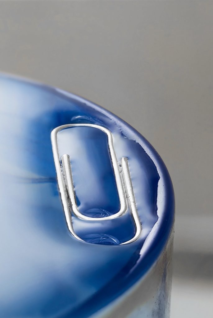 Demonstration of surface tension, a paper clip in a full, blue, glass.