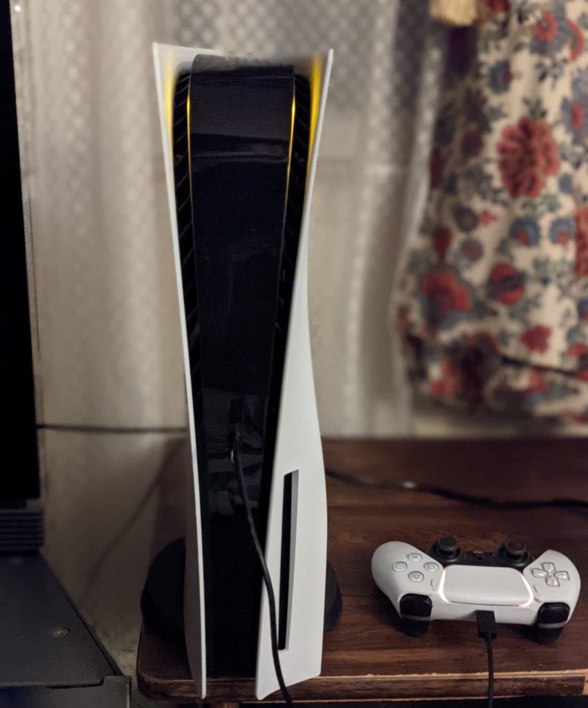 PlayStation 5 console set vertically with the stand and DualSense controller charging