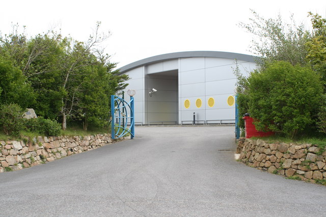 Submarine cable terminus building at Skewjack. Skewjack has a long history in telecommunications. During WWII RAF Sennen was based here because it was a good location for radio line-of-sight towards the Atlantic. 100m high masts in adjoining fields supported radar antennae as part of an early warning radar station which could detect ships and low flying aircraft up to 20 miles away in the Western Approaches. Some of the equipment was housed in camouflaged bunkers at nearby Trebehor Farm, which still exist 1302344. After the RAF station closed the accommodation buildings became Skewjack Surf Village - see the excellent website here http://www.skewjack.co.uk/. The surf village closed in the mid 1980s and nothing remains of the original buildings. This building was constructed in about 2001 as a terminus for submarine optical cables, operated by FLAG (Fiber Link Around the Globe) Telecom. The building houses the ends of two submarine fibre cables. One that crosses the Atlantic to Long Island nearly 6000km away and the other cable that crosses the channel to France in Brittany. The fibre optic cable to America is constructed with 6 fibre pairs, each capable of carrying 40 separate light wavelengths and each wavelength can carry 10GBit/s of traffic. This gives a total capacity of 2.4Tbit/s per cable making Skewjack one of the largest bandwidth communications stations in the world. The building won the 2002 CPRE RIBA Cornwall Architecture Award for Local Architects Poynton Bradbury Winter Cole.